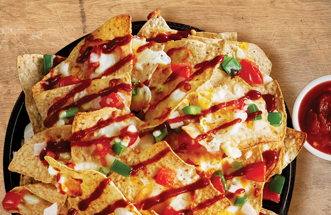 Classic BBQ Nachos with crispy chips, onions, green peppers, tomatoes, BBQ sauce and Tex-Mex cheese